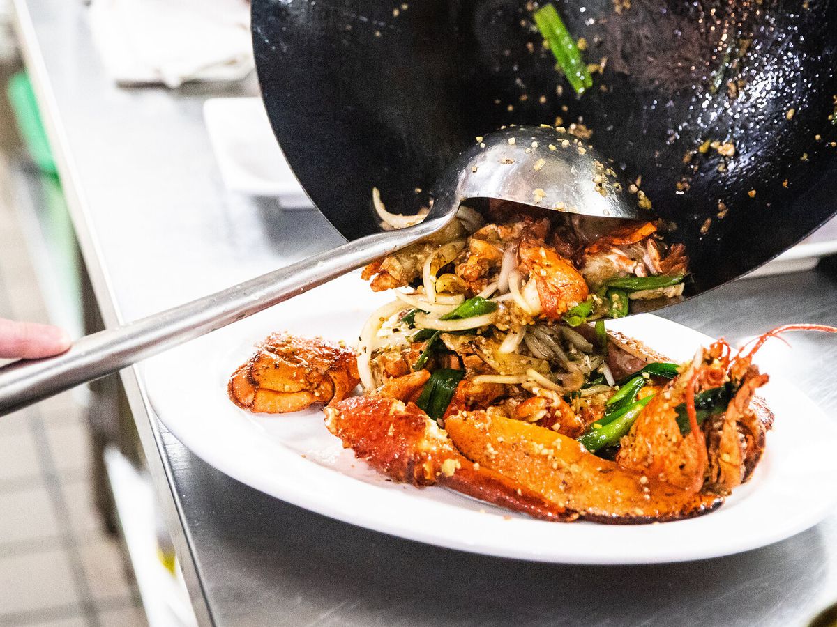 A steel ladle spooning food out of a wok onto a plate.