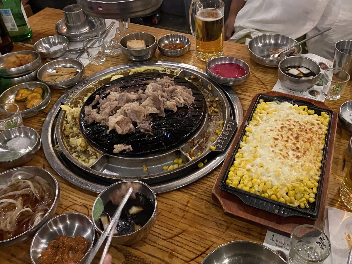 A table at a Korean barbecue restaurant adorned with meat, banchan, and cheese corn.