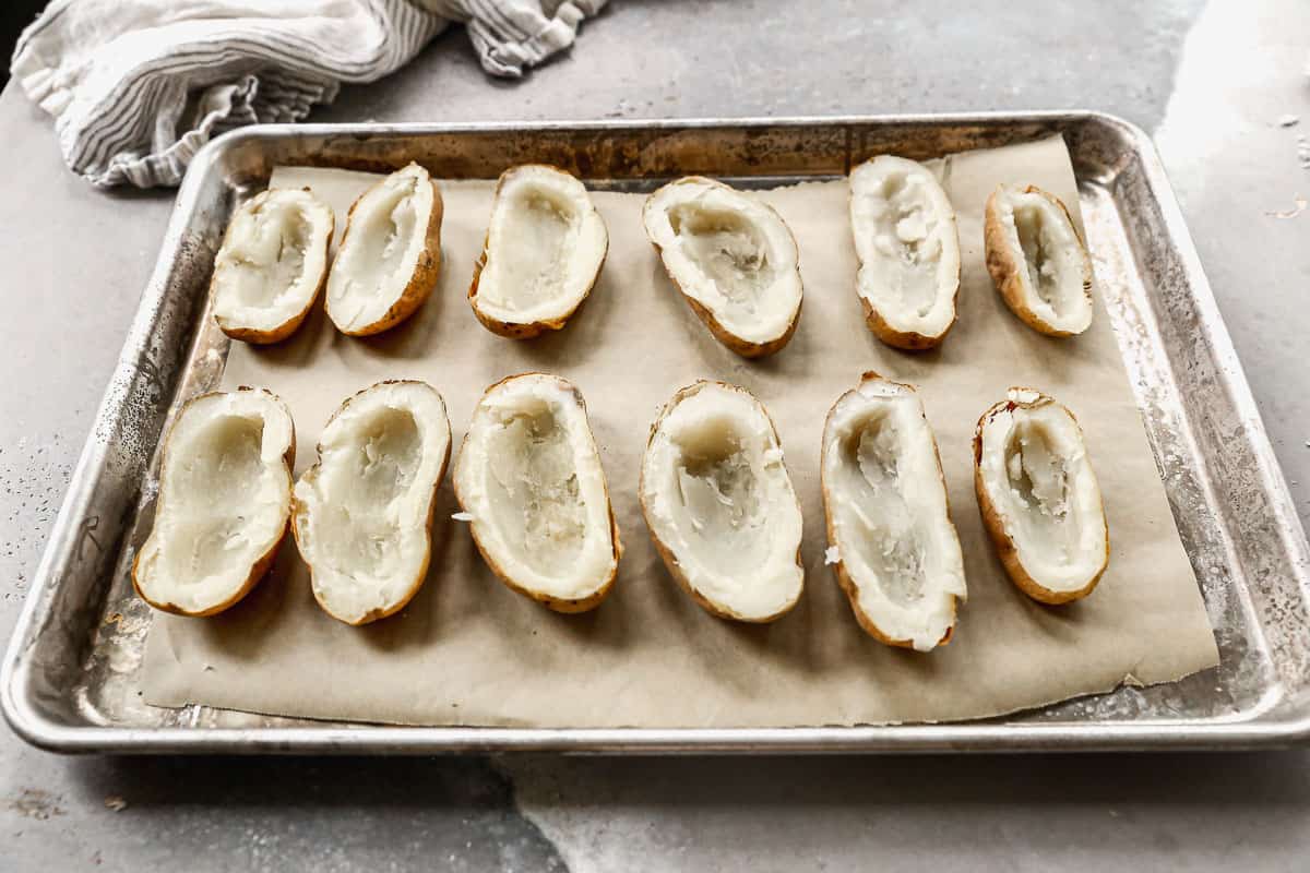 A baking sheet with parchment paper and cooked baked potatoes sliced in half.